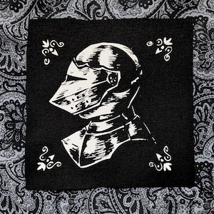 Puede incluir: Ilustración en blanco y negro de un casco de caballero en un parche de tela negro.