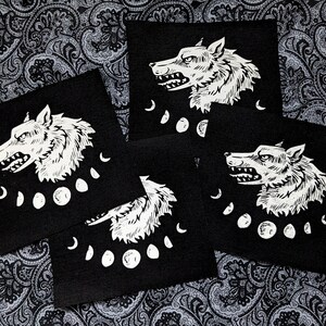 May include: Four black fabric patches featuring white wolf head illustrations and moon phases. The wolf heads are facing right and have a snarling expression. The moon phases are in a crescent shape.