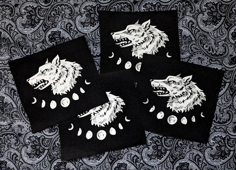May include: Four black fabric patches featuring white wolf head illustrations and moon phases. The wolf heads are facing right and have a snarling expression. The moon phases are in a crescent shape.