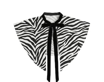 Può includere: Un colletto staccabile con motivo zebrato bianco e nero. Il colletto ha una forma a punta e include un nastro di velluto nero da annodare al centro sul davanti, fissato a una fascia in velluto nero solido attorno allo scollo.