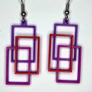 May include: A pair of earrings with three layered squares. The squares are purple, fuchsia, and red.