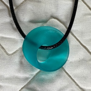 May include: A turquoise blue glass pendant with a unique, twisted shape hangs from a black cord necklace.