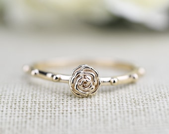 May include: A delicate gold ring with a rose-shaped design and small beads around the band.