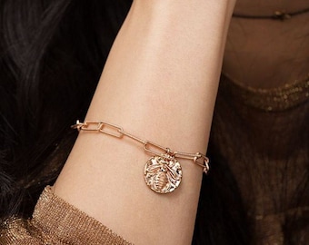 Puede incluir: Un brazalete de cadena dorada con un dije redondo que presenta un diseño de abeja texturizado.