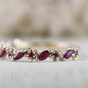 May include: A delicate gold band ring with a row of marquise-shaped ruby gemstones set in a floral design.