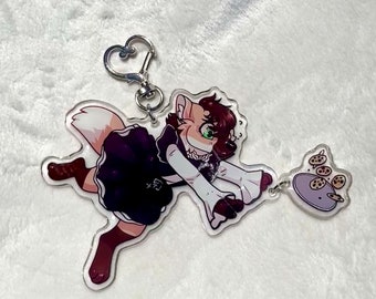 May include: A white and brown furry character wearing a black and white dress and holding a plate of cookies. The character is attached to a silver keychain.