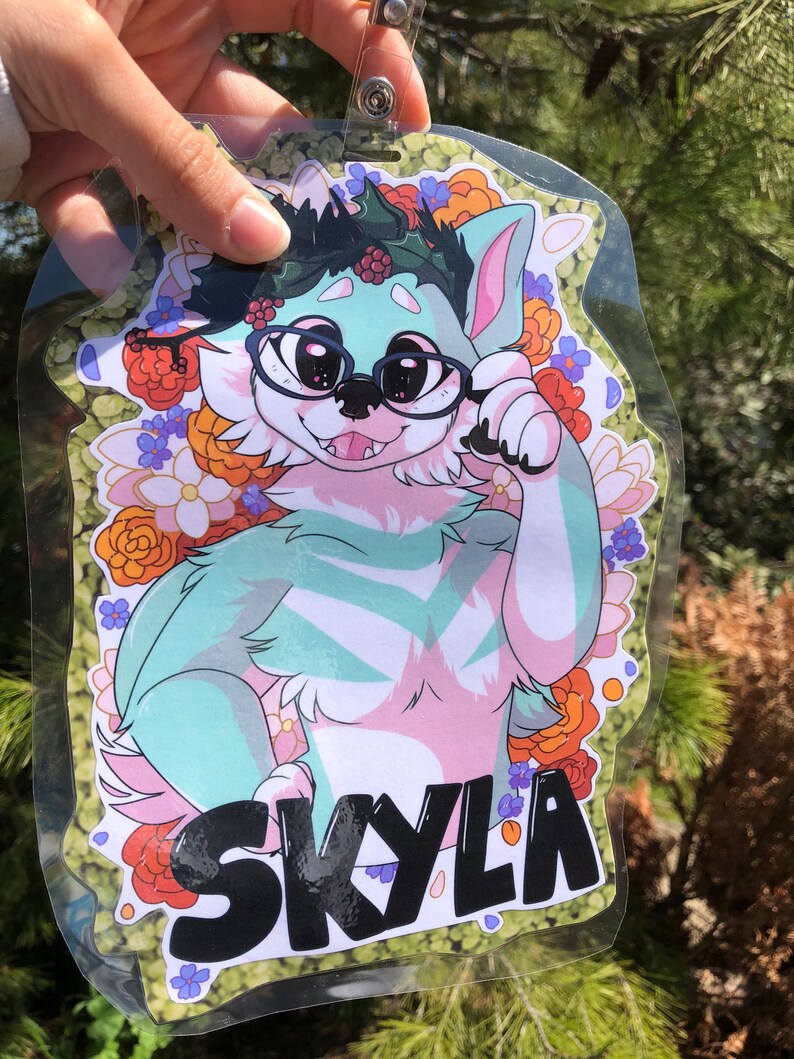 May include: A green and pink furry character with a black name tag that says "Skyla". The character is wearing glasses and a wreath of green leaves and red berries. The character is surrounded by a floral pattern of orange, red, white, and purple flowers.