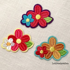 Peut inclure: Trois patchs brodés thermocollants représentant des fleurs colorées. Les patchs sont dans des tons de rose, jaune, orange, bleu et vert.