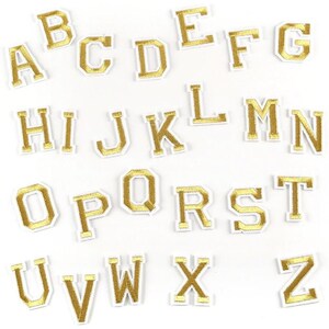 Può includere: Una collezione di lettere dell'alfabeto termoadesive dalla A alla Z. Ogni lettera presenta una finitura oro metallizzato con un bordo bianco, progettata con un carattere tipografico a blocchi classico. Le lettere sono disposte in file su sfondo bianco.
