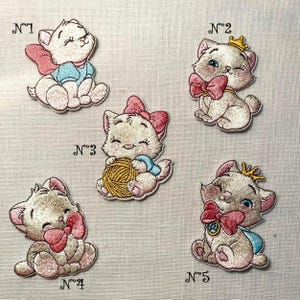 Peut inclure: Écussons brodés représentant un chaton blanc avec des nœuds roses, des accents bleus et des couronnes dorées. Les écussons sont numérotés de 1 à 5. Les écussons de chaton sont assis et ont différents accessoires.