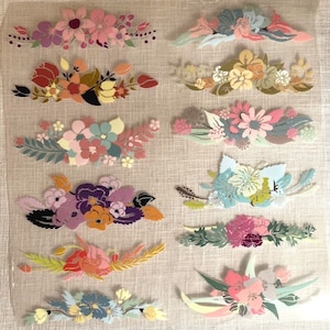 Op de afbeelding: Een verzameling van tien bloemmotieven met verschillende kleuren en patronen. De ontwerpen zijn gemaakt van stof en zijn gerangschikt in een rasterpatroon op een beige achtergrond.