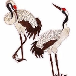 May include: Two embroidered crane patches. The cranes have white bodies, brown wings, and black legs. Each crane has a red spot on its head. One crane has its neck curved, and the other is standing upright.