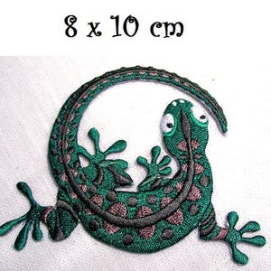 Pode incluir: Etiqueta verde bordada para passar a ferro de um gecko com a cauda enroscada, medindo 8 x 10 cm.