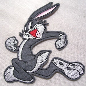 May include: A grey embroidered iron-on patch of Bugs Bunny running with his mouth open and tongue sticking out. The patch has a white outline and pink ears.