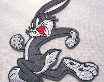 May include: A gray embroidered iron-on patch of Bugs Bunny running with his mouth open and tongue sticking out. The patch has a white outline and pink ears.