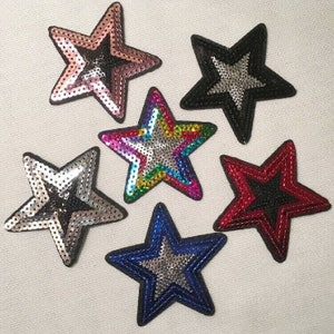 May include: Six sparkly star-shaped iron-on patches in various colors, including pink, black, rainbow, silver, red, and blue. Each star has a silver center and is made of sequins.