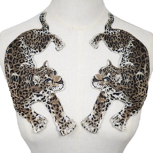 Peut inclure: Deux écussons brodés représentant des léopards. Chaque écusson montre un léopard en position d'escalade, avec un motif tacheté marron et noir. Les écussons sont conçus pour être cousus sur du tissu, ajoutant un élément décoratif aux vêtements ou accessoires.