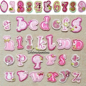 Può includere: Una collezione di lettere e numeri ricamati in tessuto rosa e bianco. Le lettere e i numeri sono decorati con disegni floreali e a spirale. I numeri sono in alto e le lettere in basso. Il testo "Loisirsetpassion" è in basso.