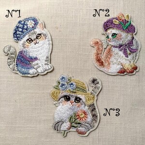 May include: Embroidered patches featuring three whimsical cat designs. Each cat wears a different hat: a blue beret, a purple hat with flowers, and a straw hat with blue flowers. The patches are numbered 1, 2, and 3.