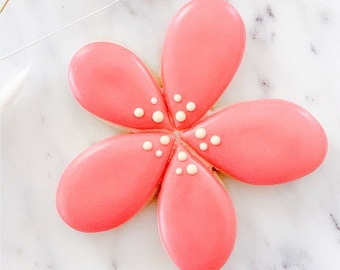 May include: A pink sugar cookie decorated with white icing dots in the shape of a flower.