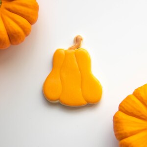 May include: Three orange pumpkins, two whole and one cut out in the shape of a pumpkin, on a white background.