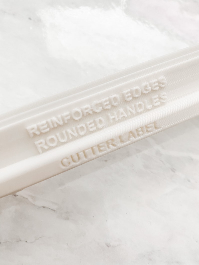 May include: White plastic rolling pin with the text "Reinforced Edges Rounded Handles Cutter Label" embossed on the side.