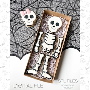 May include: A set of six cookie cutters shaped like a skeleton. The skeleton is made up of separate pieces, including the head, torso, arms, and legs. The cookie cutters are in a brown box with white tissue paper. The cookie cutters are white with black outlines.