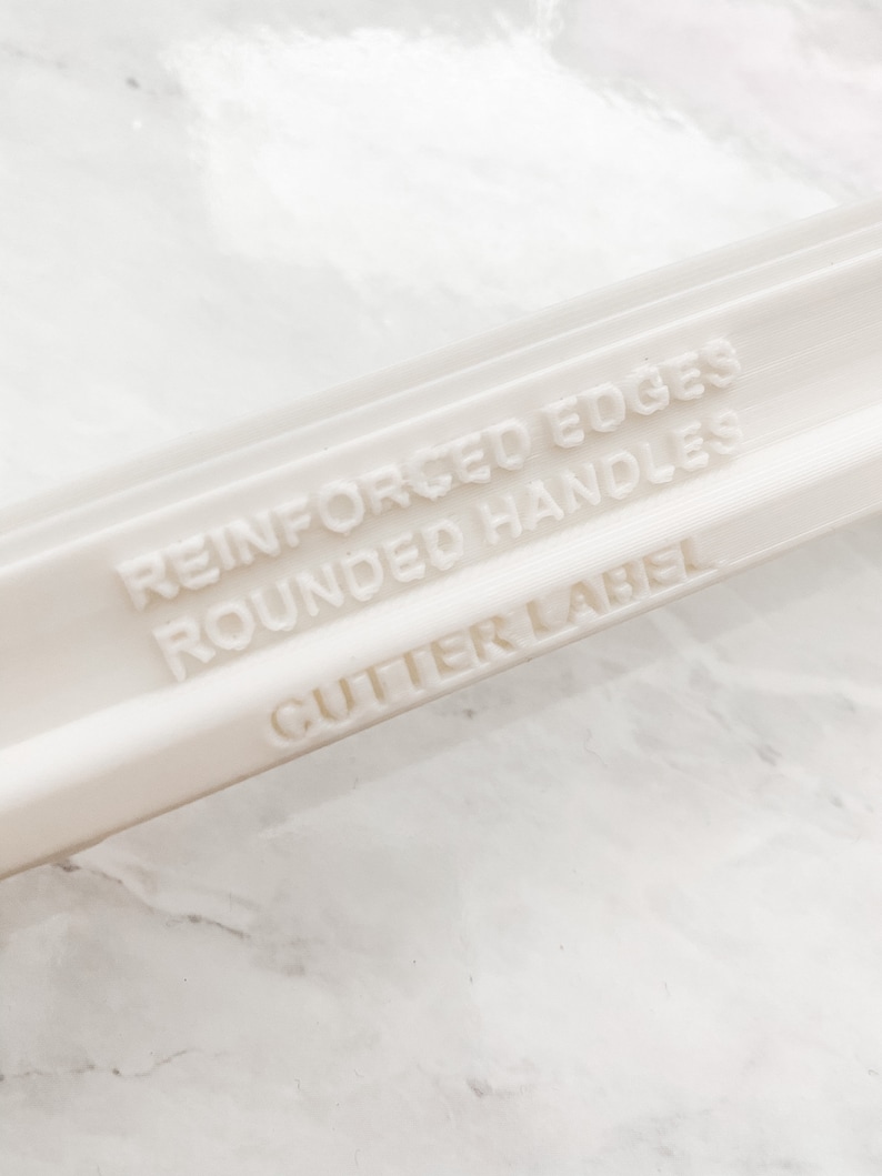 Puede incluir: Rodillo de pl&aacute;stico blanco con el texto "Reinforced Edges Rounded Handles Cutter Label" grabado en el lateral.