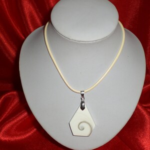 Peut inclure: Un collier avec un pendentif blanc et gris en forme de coquille avec un motif en spirale. Le collier est sur un présentoir blanc sur un fond rouge.