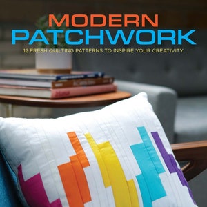 May include: A white pillow with a colorful geometric patchwork design in shades of orange, yellow, blue, pink, and purple. The pillow is on a blue couch with a wooden armrest. The text "FAVEQUILTS LEISURE ARTS the art of everyday living" is in the lower right corner of the image.
