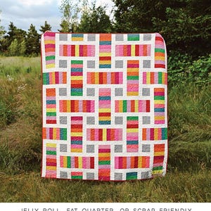 May include: A colorful quilt pattern called "The Irene Quilt" by Erica Jackman. The quilt is made with jelly roll, fat quarter, or scrap fabric. It is available in baby, lap, twin, queen, and king sizes. The quilt is displayed on a grassy field.
