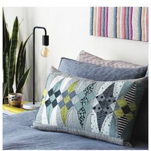 May include: A close-up of a pillow with a patchwork design in shades of blue, green, and white. The pillow is on a blue bed with a lamp and a plant in the background. The text "Temptors" and "More Glitter by Jen Kingwell" is visible at the top and bottom of the image.