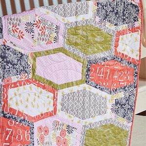 May include: A quilt pattern called "Granny Dot" with the pattern number #SGD065. The quilt is made of various fabrics in shades of pink, green, gray, and white. The quilt is made up of hexagonal shapes with different patterns and designs. The quilt is made by Swirly Girls.