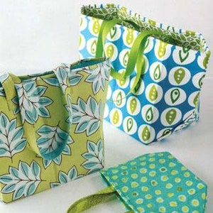 May include: Three fabric bags in different sizes and patterns. The largest bag is green with a blue leaf pattern. The medium bag is blue with a white and green pattern. The smallest bag is blue with white polka dots. The bags are all made of fabric and have handles. The text "STAND 'N STOW" is printed on the bottom of the image. The text "Atkinson Designs" and "one of life's simple pleasures" is printed at the top of the image.