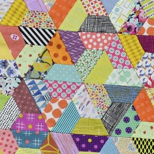 May include: A patchwork quilt featuring a dense arrangement of multi-colored fabric hexagons. The design incorporates a variety of patterns including polka dots, stripes, floral prints, and geometric shapes in vibrant shades of yellow, orange, pink, purple, green, and blue.