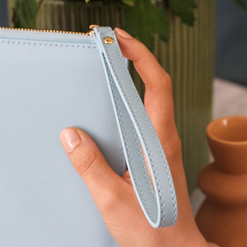 May include: A light blue clutch purse with a gold zipper and a matching light blue wrist strap.
