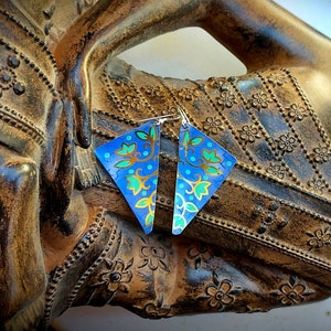 May include: A pair of triangular earrings with a blue, green and gold floral pattern. The earrings are made of metal and have a shiny finish.