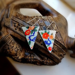 Puede incluir: Un par de pendientes triangulares con fondo blanco y un patrón floral en tonos azules, naranjas y rojos.