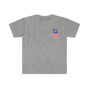 Peut inclure: Un t-shirt gris chiné avec un petit bouclier brodé sur la poitrine gauche. Le bouclier est rouge, blanc et bleu avec une étoile blanche au centre. Le texte "SHIELD UP" est imprimé en noir au-dessus du bouclier.