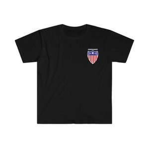 Peut inclure: T-shirt noir avec un motif de bouclier blanc représentant un drapeau américain. Le texte "#SHIELDUP" est imprimé au-dessus du bouclier.