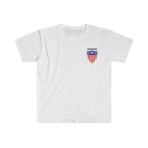 Peut inclure: T-shirt blanc avec un petit motif de bouclier brodé représentant le drapeau américain et le texte "#SHIELDUP".