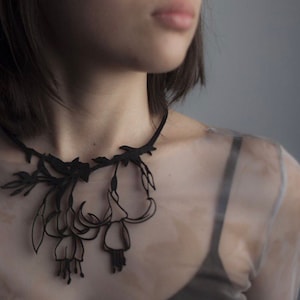 May include: A black choker necklace with a delicate floral design. The necklace is made of paper and features intricate cutouts of flowers and leaves.