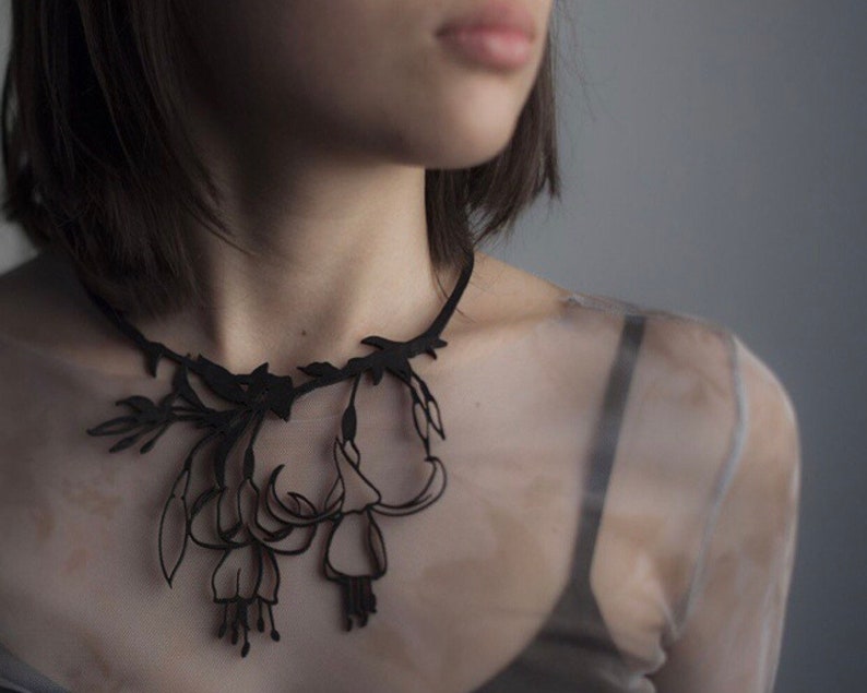 May include: A black choker necklace with a delicate floral design. The necklace is made of paper and features intricate cutouts of flowers and leaves.