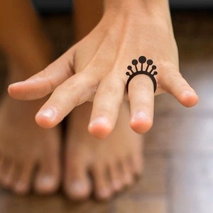 May include: A black ring tattoo on a person's finger. The ring is made of a series of connected circles with a rounded top.