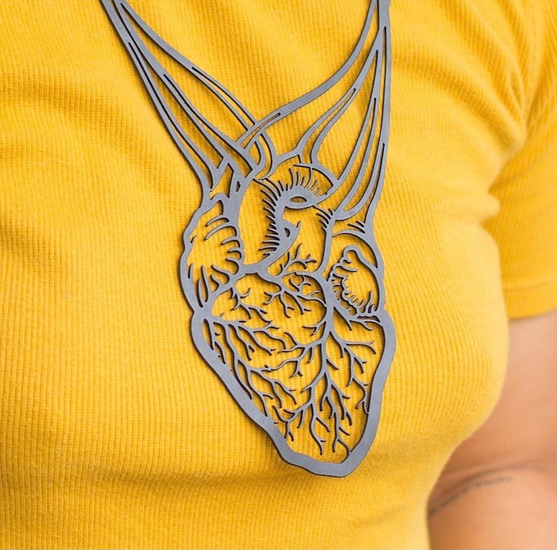 May include: A black metal necklace with a detailed anatomical heart design. The heart is intricately cut with veins and arteries.