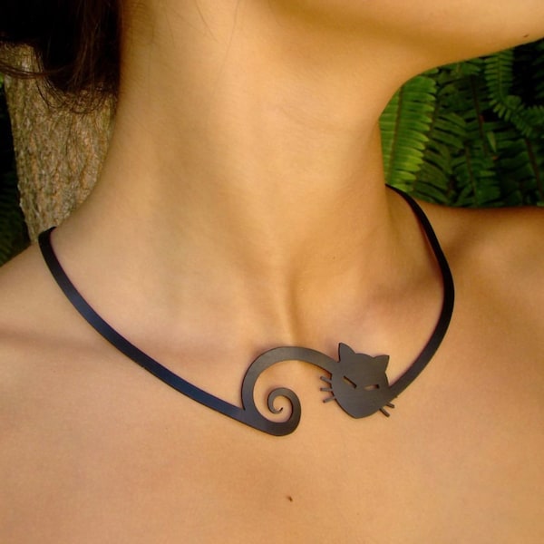 Pode incluir: Um colar de metal preto com um pingente de silhueta de gato. O gato está enroscado com a cauda formando uma espiral.