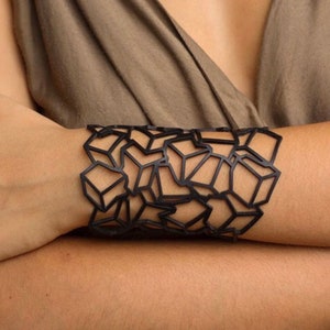 May include: A black geometric cuff bracelet with a design of interlocking squares and triangles.