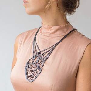 May include: A black necklace with a detailed anatomical heart pendant. The necklace is made of metal and has a delicate, intricate design.