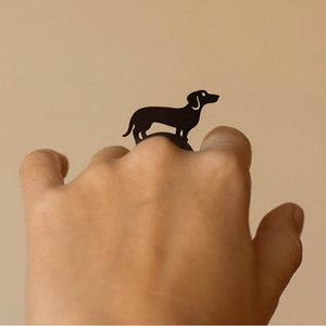 May include: A black silhouette of a dachshund dog is used as a ring on a person's finger.