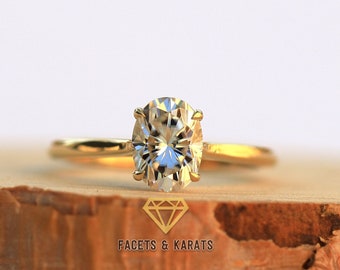May include: A gold engagement ring with a large oval-shaped diamond. The ring is sitting on a piece of wood.